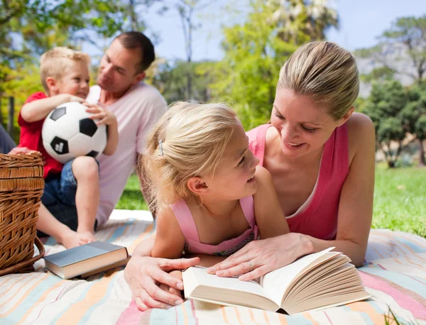 Mãe e sua filha lendo em um piquenique com sua família — Fotografia de Stock