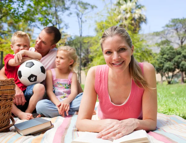 Mujer sonriente leyendo en un picnic con su familia —  Fotos de Stock
