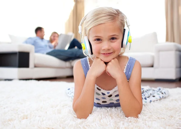 Smiling little girl listening music lying on the floor — Stock Photo, Image