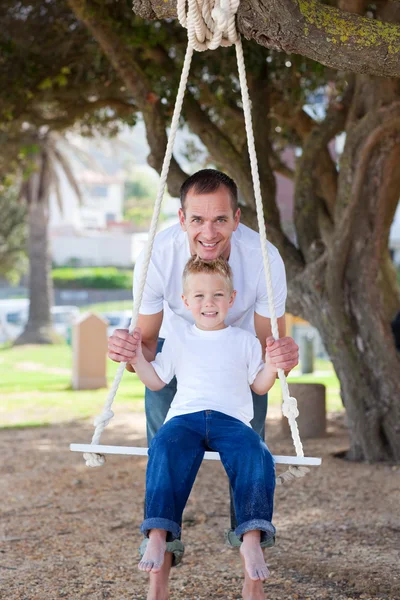 Счастливый отец толкает своего сына на качели — стоковое фото
