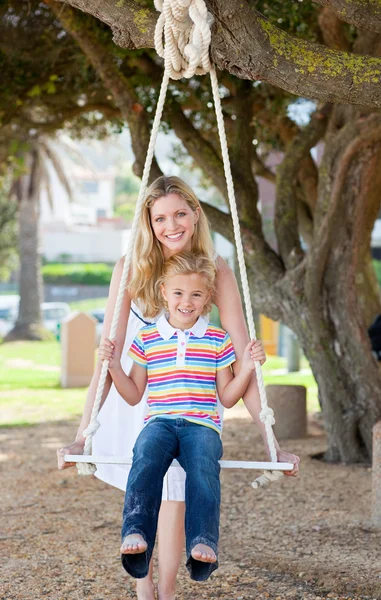 Caring mother pushing her daughter on a swing — Stock Photo, Image