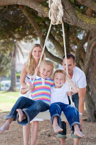Joyful parents pushing their children on a swing — Stock Photo, Image