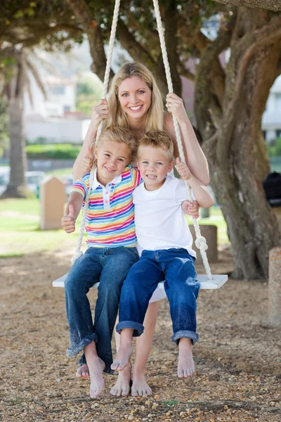 Smiling mother and her children swinging — Stock Photo, Image