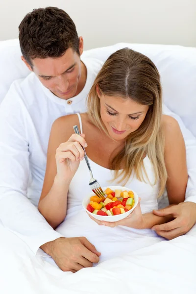 Інтимна пара їсть фрукти, що лежать на їхньому ліжку — стокове фото