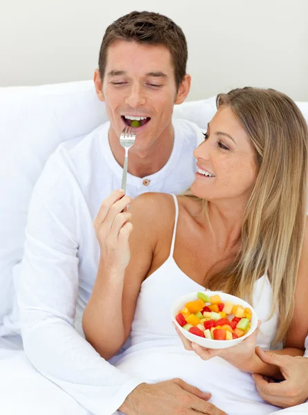 Jolly couple eating fruit lying on their bed — Stock Photo, Image