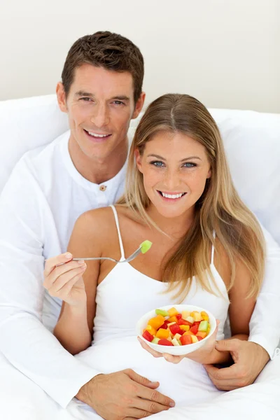 Romaantic couple eating fruit lying on their bed — Stock Photo, Image
