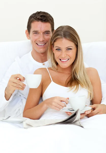 Felice coppia bere caffè sdraiato sul loro letto — Foto Stock