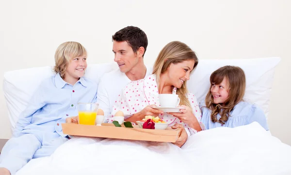 Loving family having breakfast sitting on bed — Stock Photo, Image
