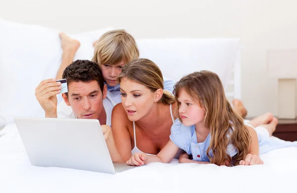 Feliz família comprando online deitado na cama — Fotografia de Stock