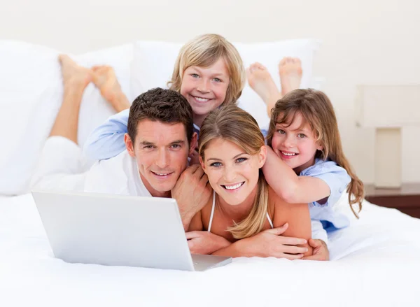 Familia sonriente mirando a un portátil acostado en la cama — Foto de Stock