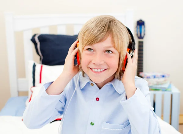 Niño feliz escuchando música sentado en la cama — Foto de Stock
