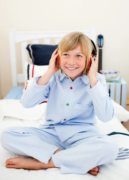 Smiling boy listening music sitting on bed — Stock Photo, Image