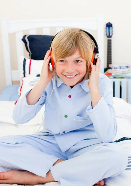 Positive boy listening music sitting on bed — Stock Photo, Image
