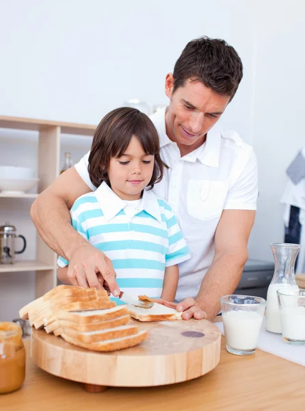 Encantador padre y su hijo extendiendo mermelada en el pan — Foto de Stock