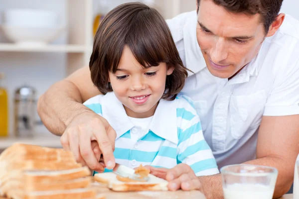 Pai amoroso e seu filho espalhando geléia no pão — Fotografia de Stock
