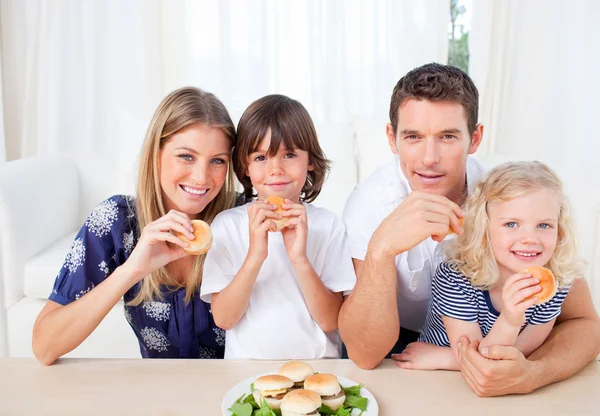 Usmívající se rodina jíst hamburgery v obývacím pokoji — Stock fotografie