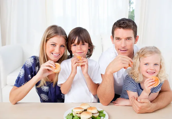 Famille souriante manger des hamburgers dans le salon — Photo