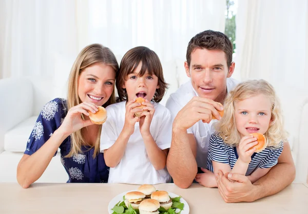 Nadšený rodina jíst hamburgery v obývacím pokoji — Stock fotografie
