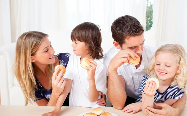 Família animada comendo hambúrgueres na sala de estar — Fotografia de Stock