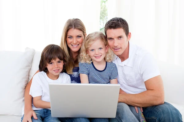 Retrato de uma família alegre usando um laptop sentado no sofá — Fotografia de Stock