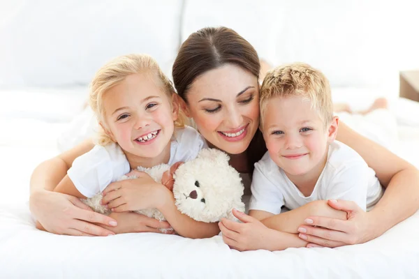 Cheerful children with their mother lying on a bed — Stock Photo, Image