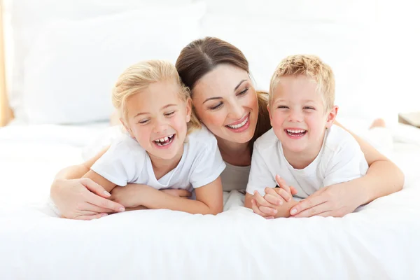 Happy siblings playing with their mother lying on a bed — Stock Photo, Image