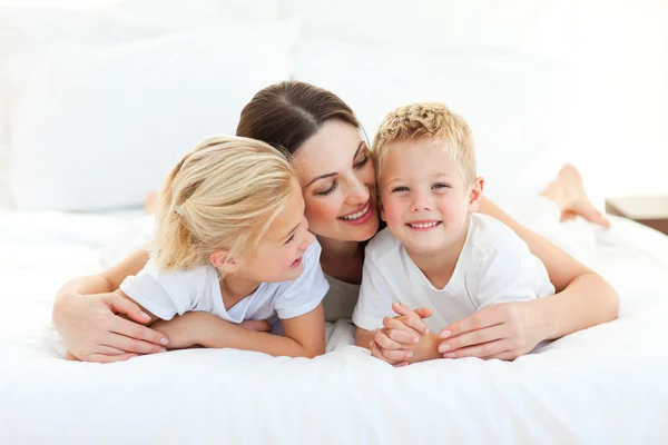 Söta barn och deras mamma som har roligt liggande på en säng — Stockfoto