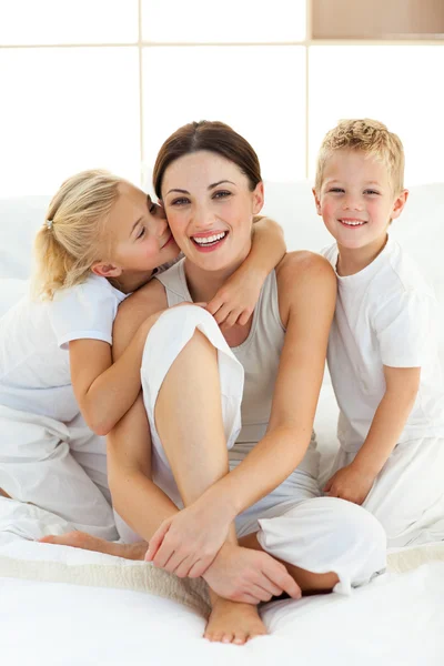 Enfants mignons embrasser leur mère assise sur un lit — Photo