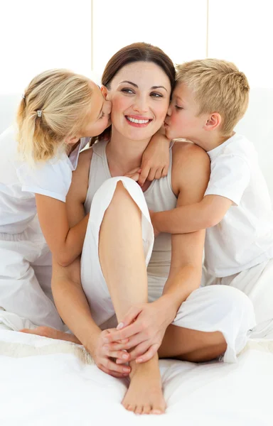 Jolly siblings kissing their mother sitting on a bed — Stock Photo, Image