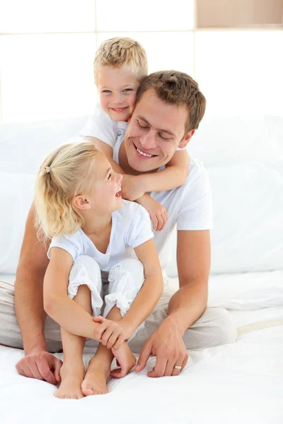 Uppmärksam attraktiva far leker med sina barn på en säng — Stockfoto