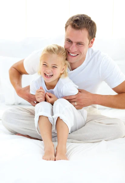 Attraktiva far leker med sin lilla flicka på en säng — Stockfoto