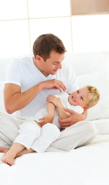 Papá animado y su pequeño niño jugando en una cama — Foto de Stock