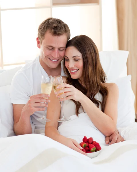 Alegre pareja bebiendo champán con fresas acostado en ser —  Fotos de Stock