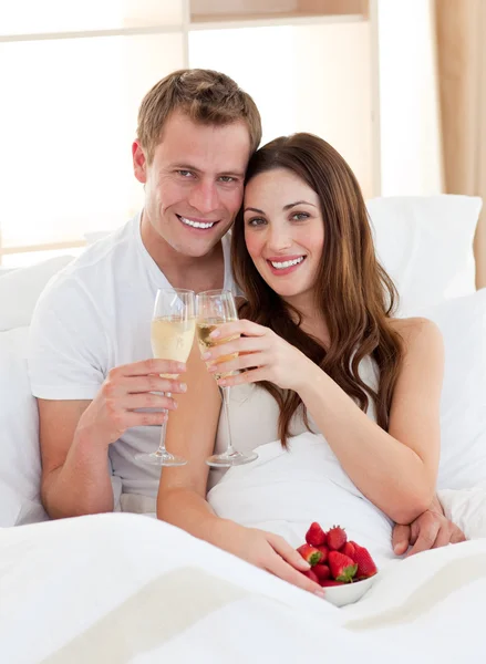 Casal apaixonado bebendo champanhe com morangos deitados em b — Fotografia de Stock