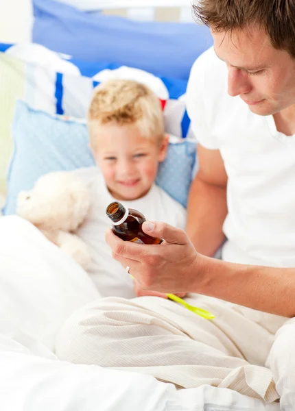 Очаровательный отец дает сироп от кашля своему больному сыну — стоковое фото