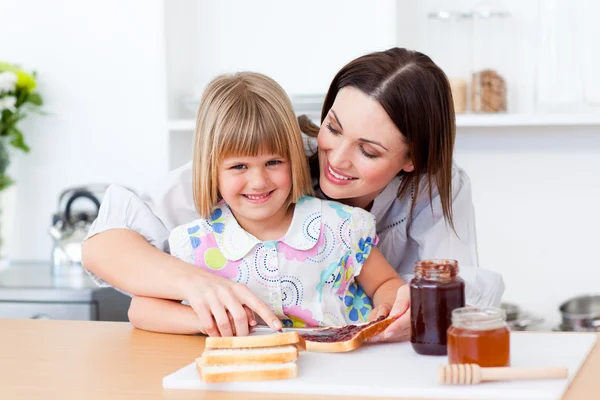 웃 고 있는 어린 소녀와 토스트를 준비 하는 그녀의 어머니 — 스톡 사진