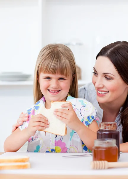 Menina feliz e sua mãe comendo fatias de pão — Fotografia de Stock