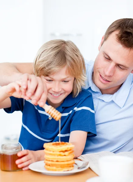 Jolly boy and his father putting honey on waffles — Stock Photo, Image