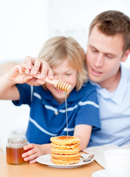 Smiling boy and his father putting honey on waffles — Stock Photo, Image
