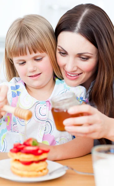 Joyful mother and her daughter putting honey on waffles — Stock Photo, Image