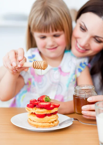 Cute little girl and her mother putting honey on waffles — Stock Photo, Image