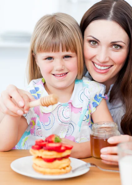 Adorable little girl and her mother putting honey on waffles — Stock Photo, Image