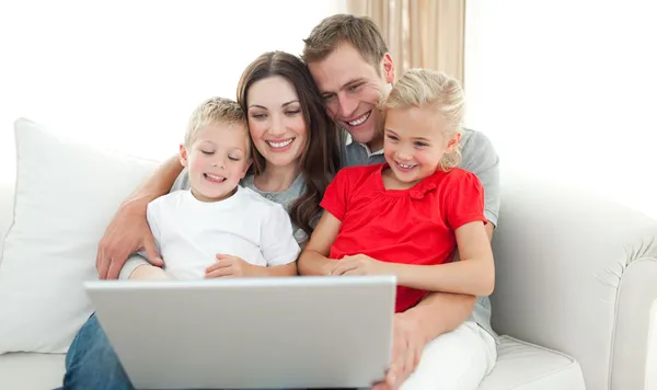Família alegre usando um computador sentado no sofá — Fotografia de Stock