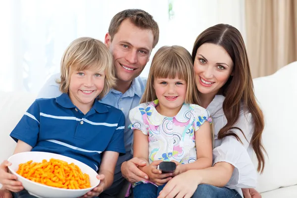 Retrato de una familia sonriente comiendo patatas fritas mientras ve la televisión —  Fotos de Stock