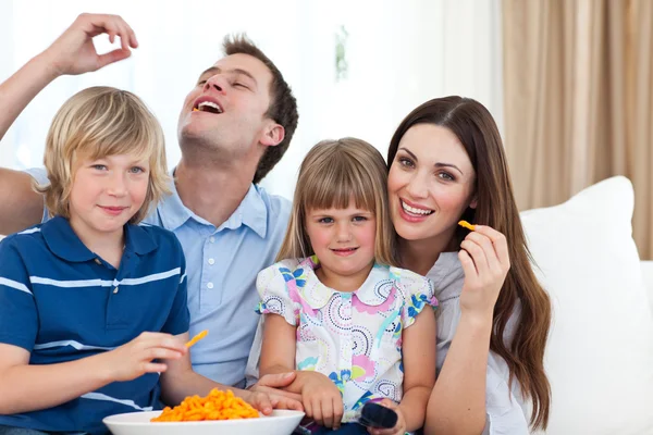 Jovem família comer batatas fritas enquanto assiste TV — Fotografia de Stock
