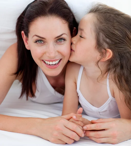 Little girl kissing her mother lying on bed — Stock Photo, Image