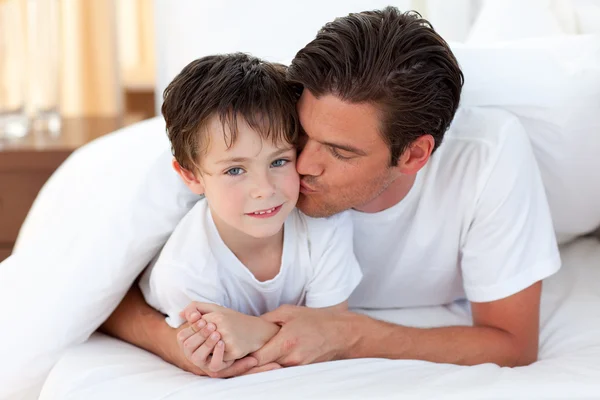 Батько цілує сина, що лежить на ліжку — стокове фото