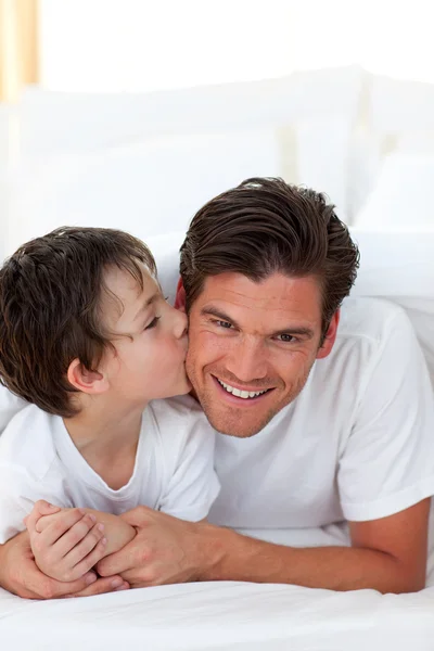 Little boy kissing his father lying on bed — Stock Photo, Image