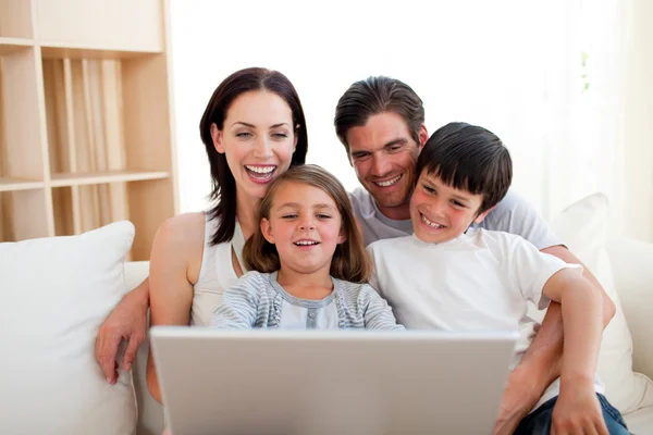 Sonriendo fanáticamente usando un portátil en el sofá — Foto de Stock