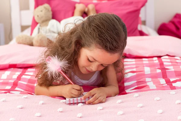 Nahaufnahme eines kleinen Mädchens, das auf dem Bett schreibt — Stockfoto